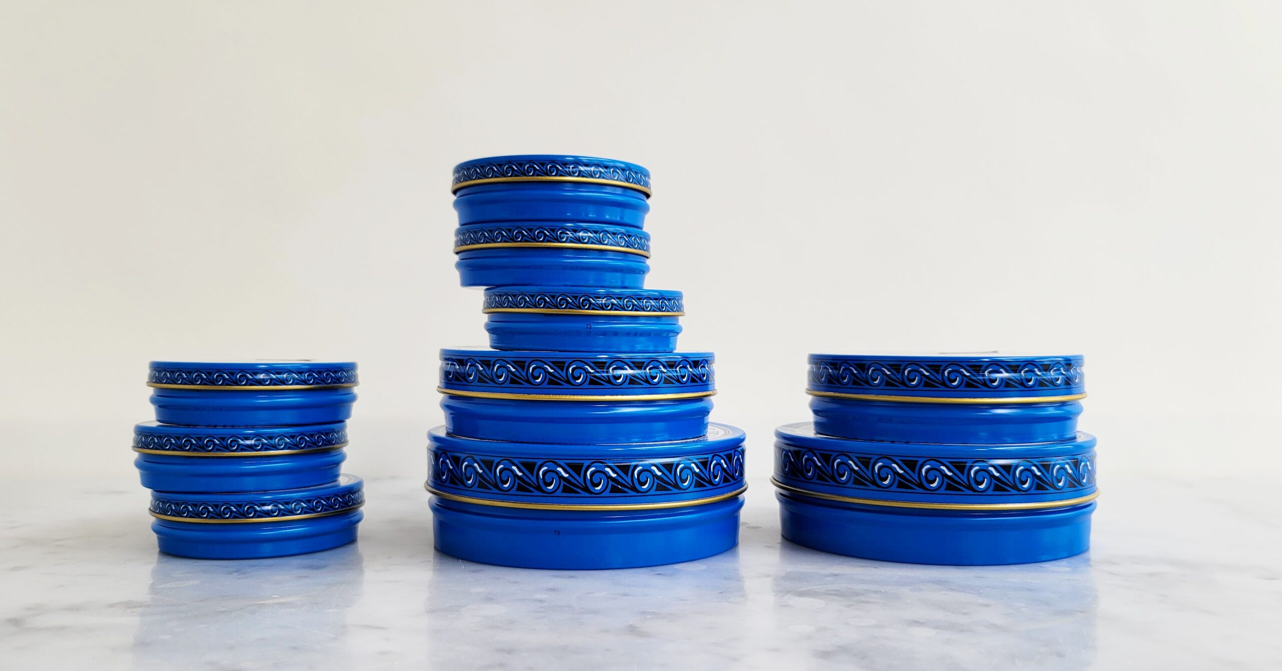 Many blue tins of Petrossian Caviar sit in three stacks of differing heights on a white marble counter top.