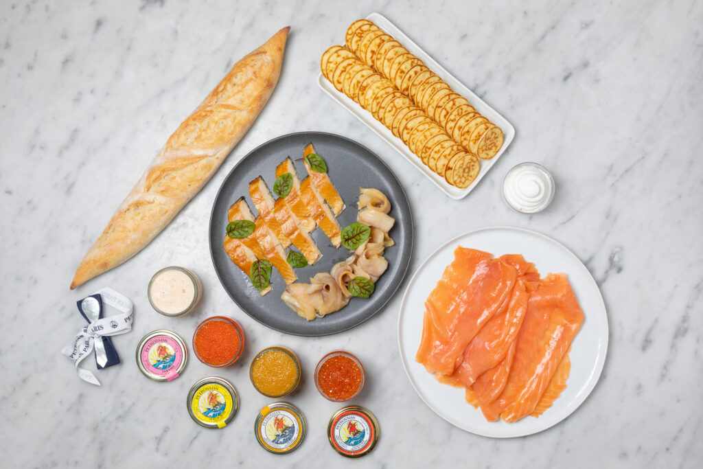 a white countertop where delicious Petrossian products are laid out on display, including blinis, smoked salmon, taramas and salmon roe.