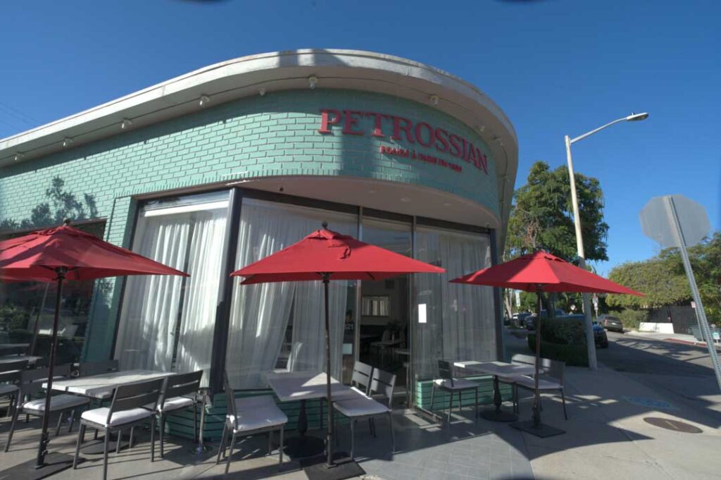 an elegant storefront with tables and umbrellas outside on a sunny day. the building says "Petrossian" in red letters over the door.